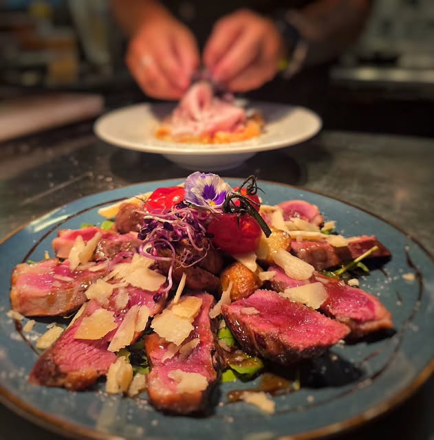 Le chef dresse une assiette de viande rosée aux copeaux de parmesan et fleurs comestibles