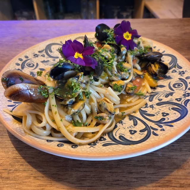Linguine aux moules décorées de pensées sur une assiette en faïence bleue