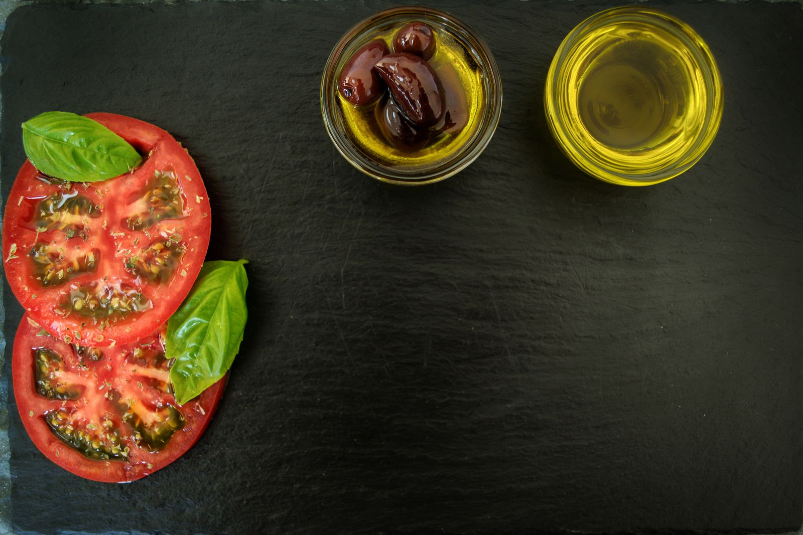 Tranches de tomate, basilic et huile d'olive sur une ardoise